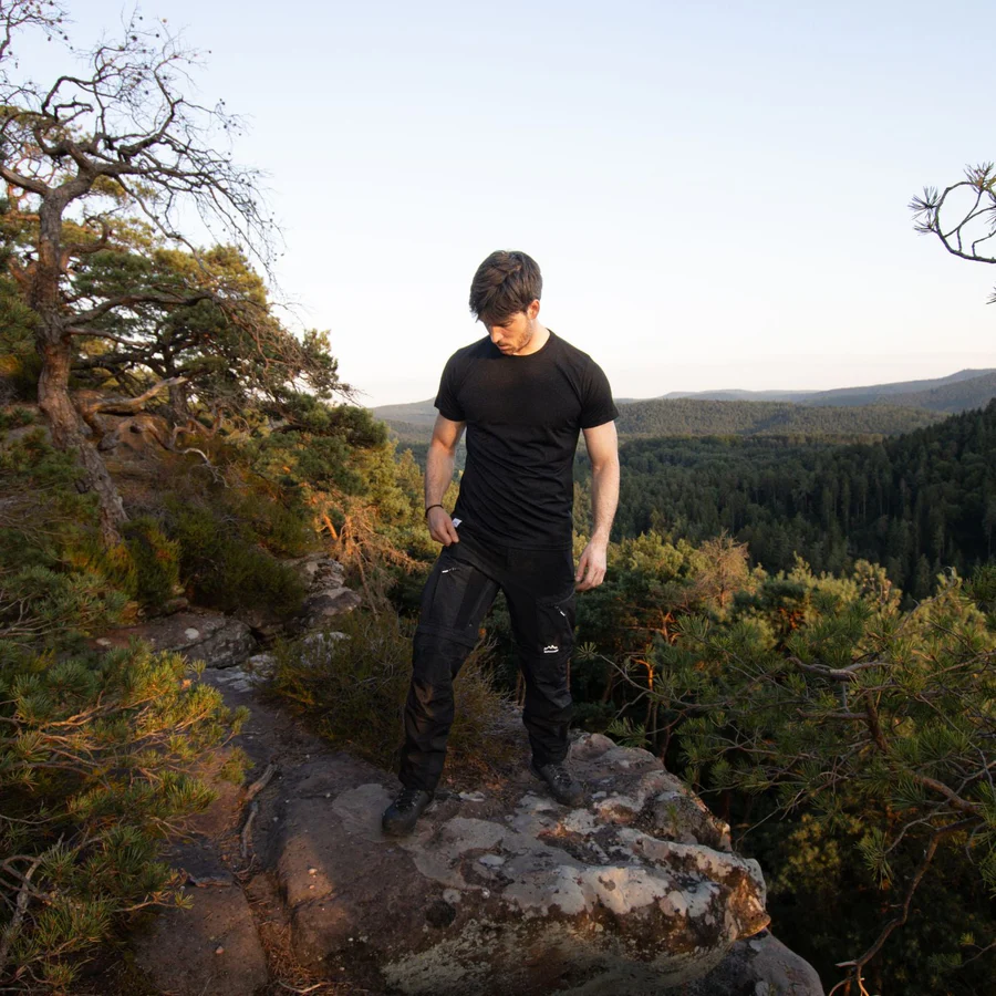 Mann mit dem Alpenwert Merino Shirt auf einem Felsen in den Bergen